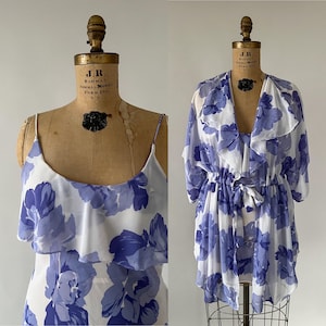 Op de afbeelding: Een witte en blauwe bloemenprint badjas met een bijpassende slip. De badjas heeft een strik in de taille en een gerimpelde halslijn. De slip heeft een gerimpelde halslijn en dunne bandjes.