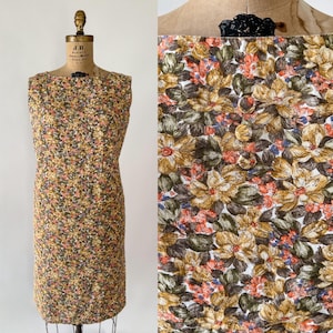 May include: A sleeveless, knee-length dress with a floral pattern in shades of yellow, brown, green, and peach. The dress is displayed on a vintage dress form. A fabric swatch with the same floral pattern is shown next to the dress.