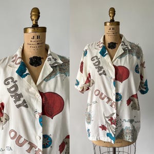 May include: A white short-sleeved button-up shirt with a map print and the text "G'DAY OUT" on it. The shirt has a blue, red, and green color scheme.