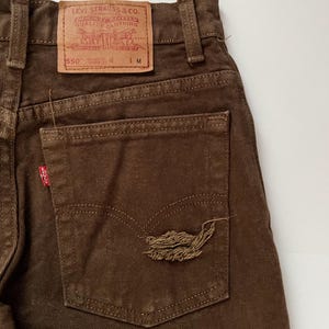 Puede incluir: Vaqueros de mezclilla marr&oacute;n con un parche de Levi Strauss & Co. en el bolsillo trasero. El parche tiene el texto "Levi Strauss & Co.  San Francisco, Cal.  Original  Quality Clothing  Trade Mark  Registered  550" y "L.M.".