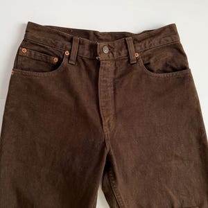 Puede incluir: Un par de pantalones vaqueros de color marr&oacute;n con un dise&ntilde;o cl&aacute;sico de cinco bolsillos.