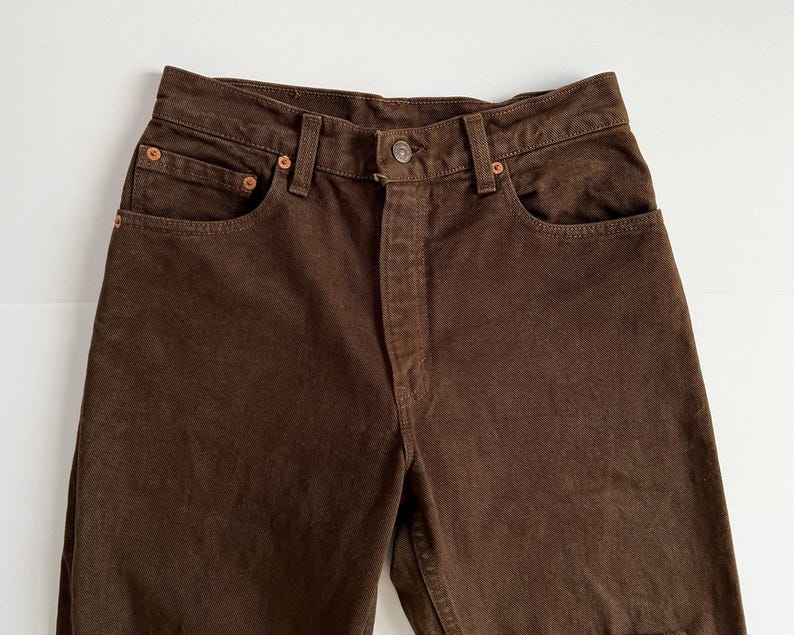 Puede incluir: Un par de pantalones vaqueros de color marr&oacute;n con un dise&ntilde;o cl&aacute;sico de cinco bolsillos.