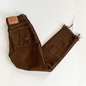 Puede incluir: Vaqueros de mezclilla marr&oacute;n con dobladillo deshilachado y un parche de Levi's en la parte posterior. Los vaqueros tienen un aspecto desgastado con un peque&ntilde;o agujero en el bolsillo trasero.