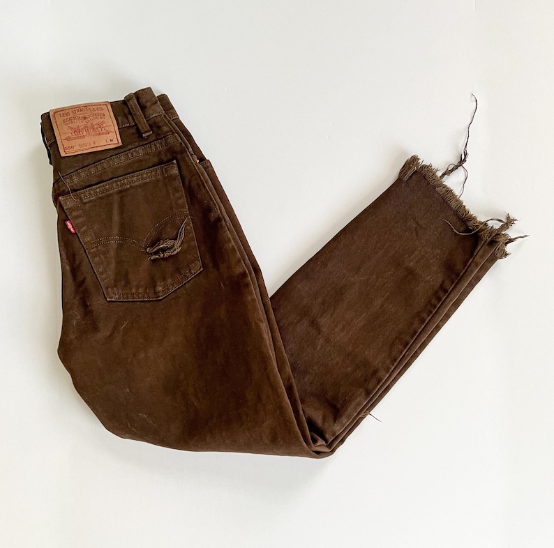 Puede incluir: Vaqueros de mezclilla marr&oacute;n con dobladillo deshilachado y un parche de Levi's en la parte posterior. Los vaqueros tienen un aspecto desgastado con un peque&ntilde;o agujero en el bolsillo trasero.