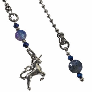 May include: Two silver-toned ceiling fan pull chains. One chain features a silver unicorn charm, a blue and purple marbled bead, and blue crystal accents. The other chain has a blue bead and crystal accents.
