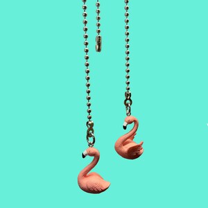 May include: Two pink flamingo fan pull chains hanging from silver chains against a turquoise background.