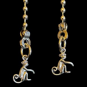 May include: Two silver monkey pull chains with a ball chain. Each monkey is sitting with its tail curled around its legs.