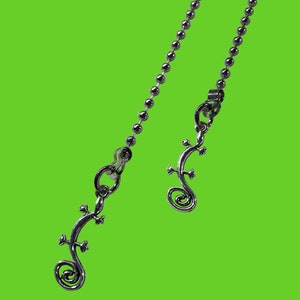 May include: A silver chain necklace with two lizard-shaped pendants. The chain is made of small, round beads.