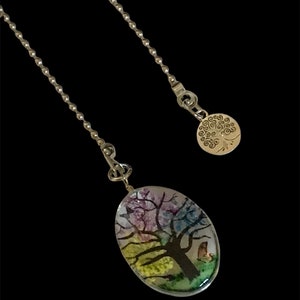 May include: A silver chain necklace with a round pendant featuring a tree of life design and a second oval pendant with a colorful tree and a bird inside.