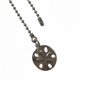 May include: A silver-toned ceiling fan pull chain with a decorative, circular pendant. The pendant features a flower-like design with cut-out details. The chain is made of small, connected metal balls.