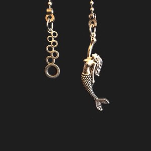 May include: A silver chain necklace with a mermaid charm. The chain is made of small, round beads. The mermaid charm is detailed and has a flowing tail.