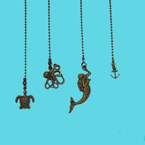 May include: Four gold-toned metal fan pull chains with different sea creature charms: a turtle, an octopus, a mermaid, and an anchor. The chains are hanging against a light blue background.
