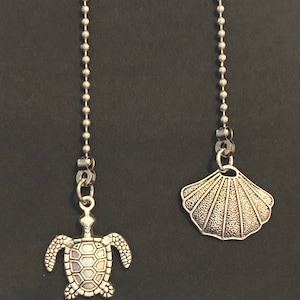 May include: Two silver chain pulls with decorative ends. One end features a silver turtle with a pearlescent shell. The other end features a silver seashell.