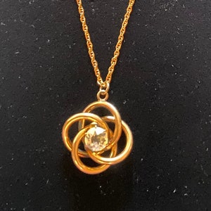 May include: A gold chain necklace with a pendant featuring a clear crystal set in a gold flower design.