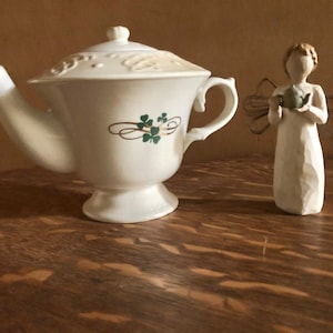 May include: White ceramic teapot with a green shamrock design and a white porcelain angel figurine holding a small teapot.