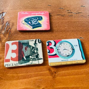 May include: Three vintage-style rectangular magnets. One features a rotary phone with the text "Hello... everybody!". Another displays a vintage camera with the word "SPECIAL" and the number "23". The third shows a clock with the text "MIMIMASTER" and the price $7.95.
