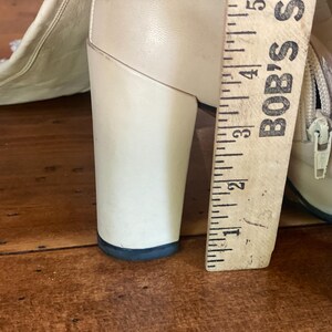 May include: Close-up of a cream-colored boot with a chunky heel. A wooden ruler, marked with inches, is placed next to the heel. The heel measures approximately 3 inches in height.
