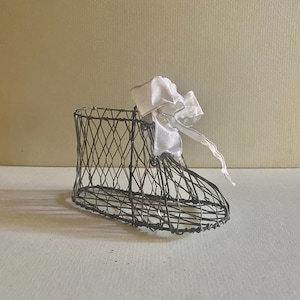 May include: A wire mesh baby shoe with a white satin bow. The shoe is a decorative item and is not intended for use as footwear.