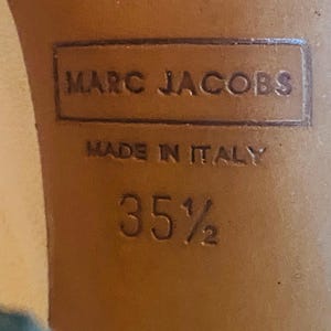 May include: Close-up of a shoe sole with the embossed text "MARC JACOBS" and "MADE IN ITALY". The size is indicated as "35 1/2". The sole is a light brown color.