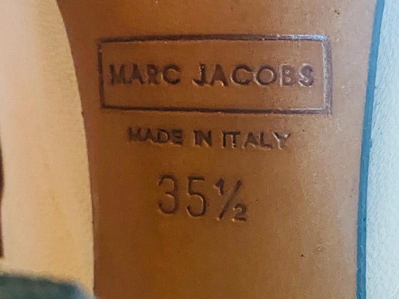 May include: Close-up of a shoe sole with the embossed text "MARC JACOBS" and "MADE IN ITALY". The size is indicated as "35 1/2". The sole is a light brown color.