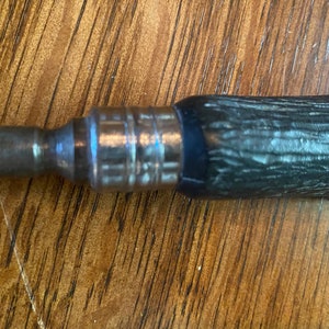 May include: A close-up of a silver and black screwdriver with a wooden handle. The handle has a textured pattern.
