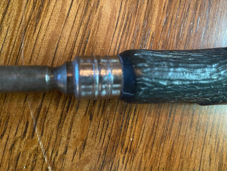 May include: A close-up of a silver and black screwdriver with a wooden handle. The handle has a textured pattern.