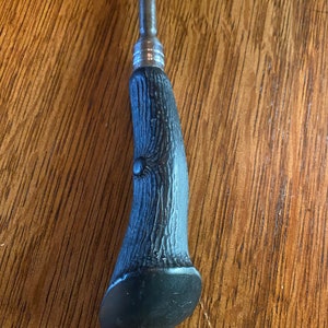 May include: A black and silver metal handle with a textured, wood-like design. The handle is shaped like a curved horn.
