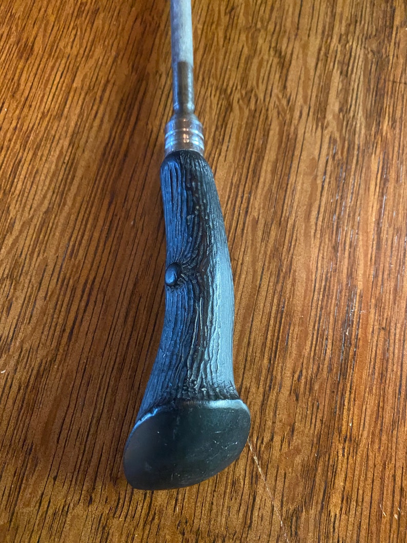 May include: A black and silver metal handle with a textured, wood-like design. The handle is shaped like a curved horn.