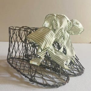 May include: A pair of wire baby shoes with a green and white striped ribbon bow. The shoes are made of wire and are shaped like baby shoes. The ribbon is tied in a bow on top of the shoes.