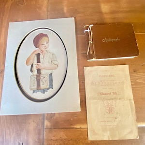 Könnte beinhalten: Ein oval gerahmter Druck eines jungen Jungen mit roter Mütze und gestreiftem Hemd, der ein Buch mit der Aufschrift "Primer" hält. Ein braunes Autogrammbuch und ein Abschlussfeierprogramm aus dem Jahrgang '88 sind ebenfalls vorhanden.