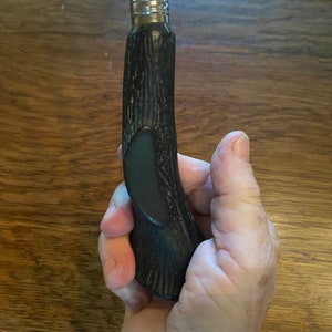 May include: A black and silver bottle opener with a wooden handle. The handle has a textured surface and a dark green accent.
