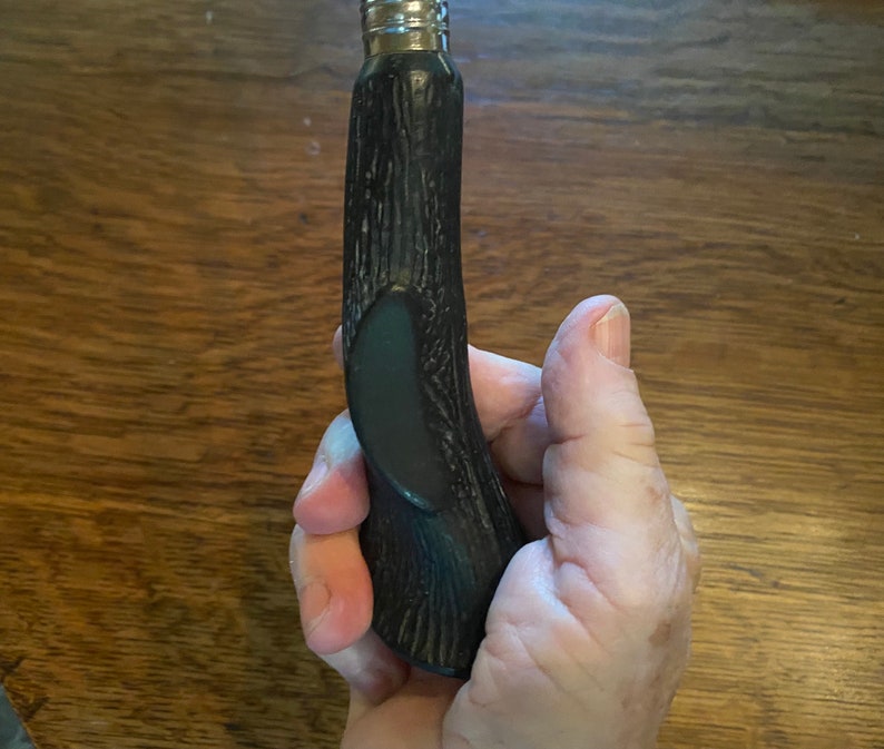 May include: A black and silver bottle opener with a wooden handle. The handle has a textured surface and a dark green accent.