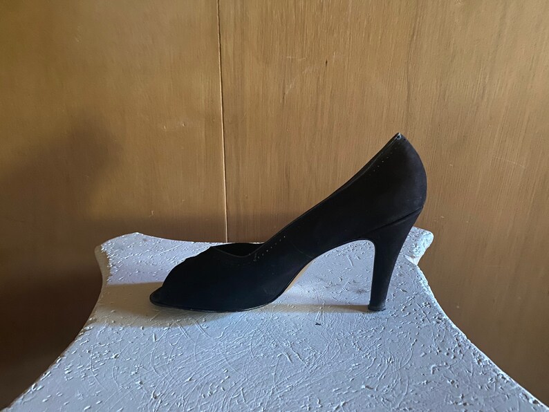 Op de afbeelding: Een zwarte su&egrave;de peep-toe pumps met een stilettohak.