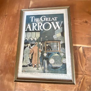 Könnte beinhalten: Eine gerahmte Vintage-Werbung für The Great Arrow, eine Autofirma. Die Anzeige zeigt eine Schwarzweißillustration eines Autos mit Menschen, die darum herumstehen. Der Text "The Great Arrow" steht in großen, fetten Buchstaben oben in der Anzeige. Der Text "The Saxon B. Pierce Company, Members of the A.L.A.M. Buffalo, New York" steht unten in der Anzeige.