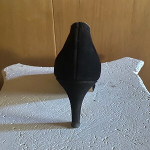 Op de afbeelding: Zwarte su&egrave;de pumps met hoge hak en spitse neus.