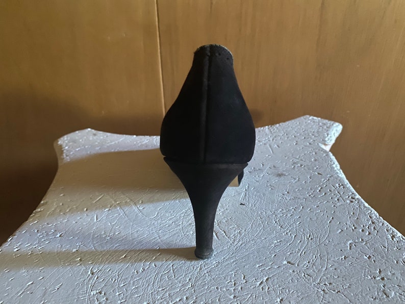 Op de afbeelding: Zwarte su&egrave;de pumps met hoge hak en spitse neus.