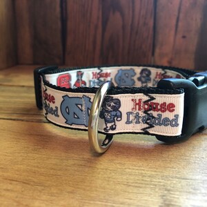 K&ouml;nnte beinhalten: Wei&szlig;er Hundehalsband mit einer schwarzen Schnalle und einem silbernen Ring. Das Halsband hat einen wei&szlig;en Hintergrund mit einem blauen und roten Design und dem Text "House Divided".