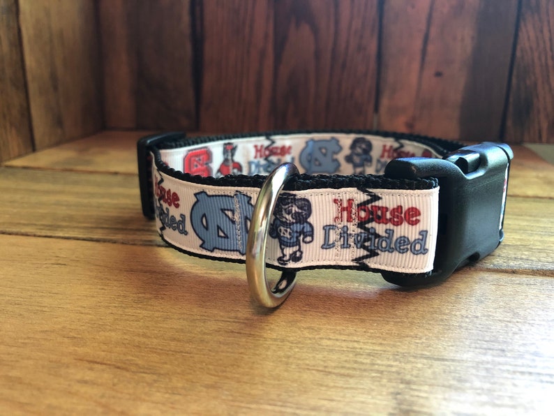 K&ouml;nnte beinhalten: Wei&szlig;er Hundehalsband mit einer schwarzen Schnalle und einem silbernen Ring. Das Halsband hat einen wei&szlig;en Hintergrund mit einem blauen und roten Design und dem Text "House Divided".