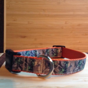 May include: A camouflage dog collar with an orange trim and a silver metal D-ring.