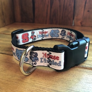 K&ouml;nnte beinhalten: Ein wei&szlig;es Hundehalsband mit einer schwarzen Schnalle und einem silbernen Ring. Das Halsband hat ein sich wiederholendes Muster mit den Worten "House Divided" und Bildern der Maskottchen der University of North Carolina und der North Carolina State University.