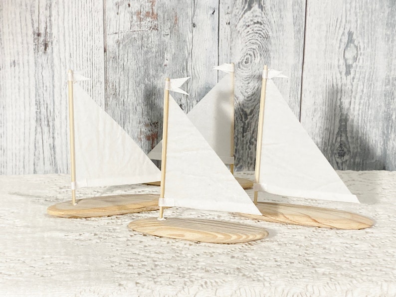 Puede incluir: Tres veleros de madera en miniatura con velas blancas sobre un mantel de encaje blanco. Los veleros est&aacute;n hechos de madera natural y tienen un dise&ntilde;o sencillo.