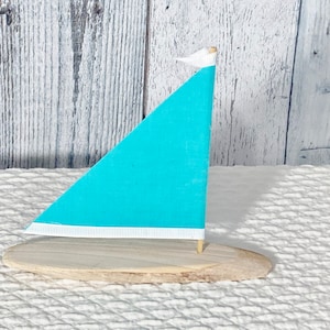 May include: A small wooden sailboat with a turquoise sail and a white trim. The sail is attached to a wooden mast and the boat is sitting on a wooden base.