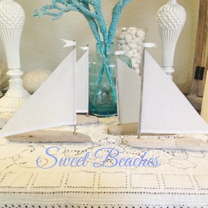 Puede incluir: Dos veleros blancos hechos de madera a la deriva y tela, con velas blancas, se exhiben sobre un mantel de encaje blanco. Los veleros est&aacute;n sobre una mesa con velas y otras decoraciones.