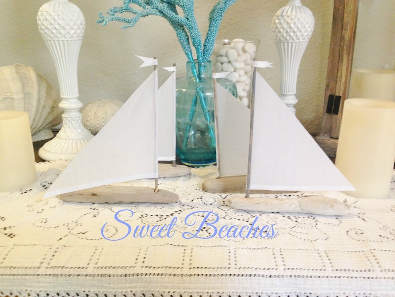 Puede incluir: Dos veleros blancos hechos de madera a la deriva y tela, con velas blancas, se exhiben sobre un mantel de encaje blanco. Los veleros est&aacute;n sobre una mesa con velas y otras decoraciones.