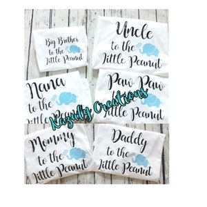 May include: Five white t-shirts with black text and a blue elephant graphic. The shirts read "Big Brother to the Little Peanut", "Nana to the Little Peanut", "Uncle to the Little Peanut", "Paw Paw to the Little Peanut", "Mommy to the Little Peanut", and "Daddy to the Little Peanut".