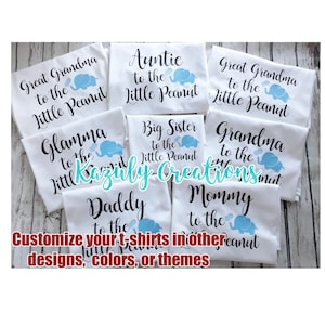 May include: A set of white t-shirts with blue and black text and images of elephants. The shirts say "Great Grandma to the Little Peanut", "Auntie to the Little Peanut", "Big Sister to the Little Peanut", "Glamma to the Little Peanut", "Grandma to the Little Peanut", "Daddy to the Little Peanut", and "Mommy to the Little Peanut".