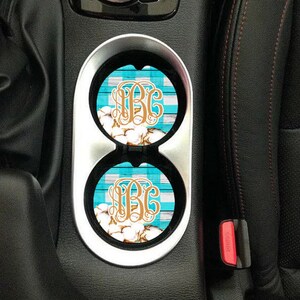 May include: Two car coasters with a blue and white checked pattern and a gold monogram. The coasters are in a car cup holder.