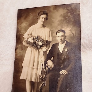 Novia y novio jóvenes posando para su foto de boda. Ramo de flores vivas. Postal en estado sin uso. Sin marcas ni daños.