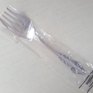 May include: A silver fork with an ornate handle, packaged in a clear plastic bag. The bag has the text "Grand Manor by Smith's" printed on it.