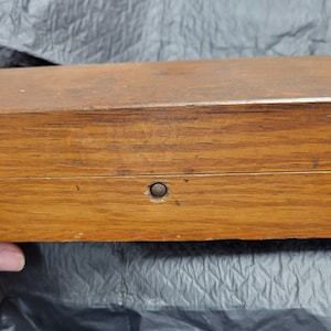 May include: A wooden box with a hinged lid and a small metal knob on the front. The box is made of light brown wood and has a natural finish.